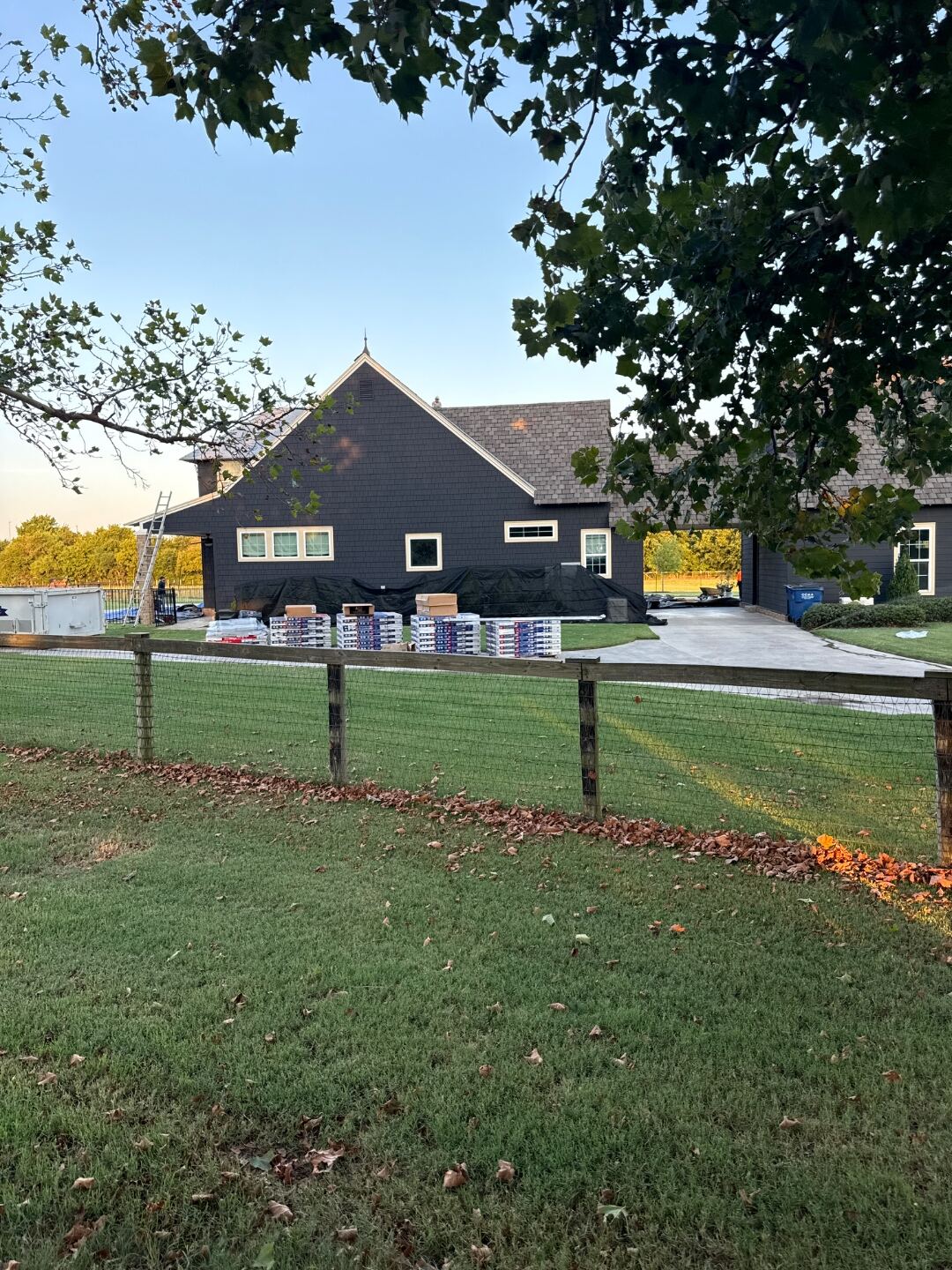 Completed re-roof on a two-story Oklahoma home with dark architectural shingles, new shingle pallets stacked neatly out front.