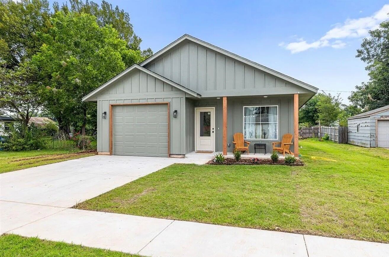 Gray board-and-batten home exterior with covered porch and Adirondack chairs, finished construction work.
