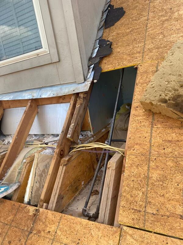 Opening in a roof deck during storm damage repair, with exposed rafters, sheathing removed, and clear blue Oklahoma sky overhead.