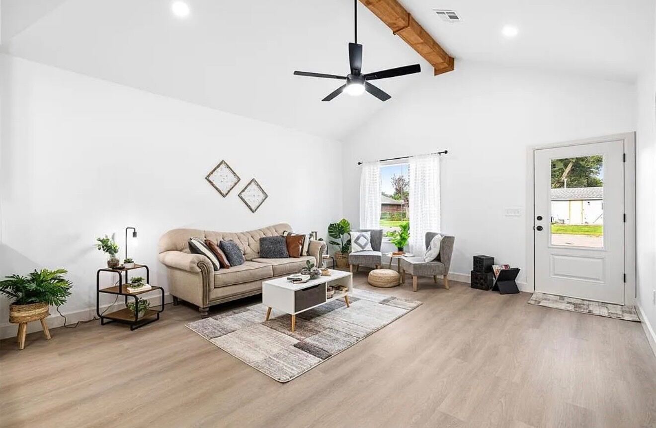 Clean vaulted living room with exposed beam, built-ins, and natural light — interior work by Genesis Roofing and Construction.