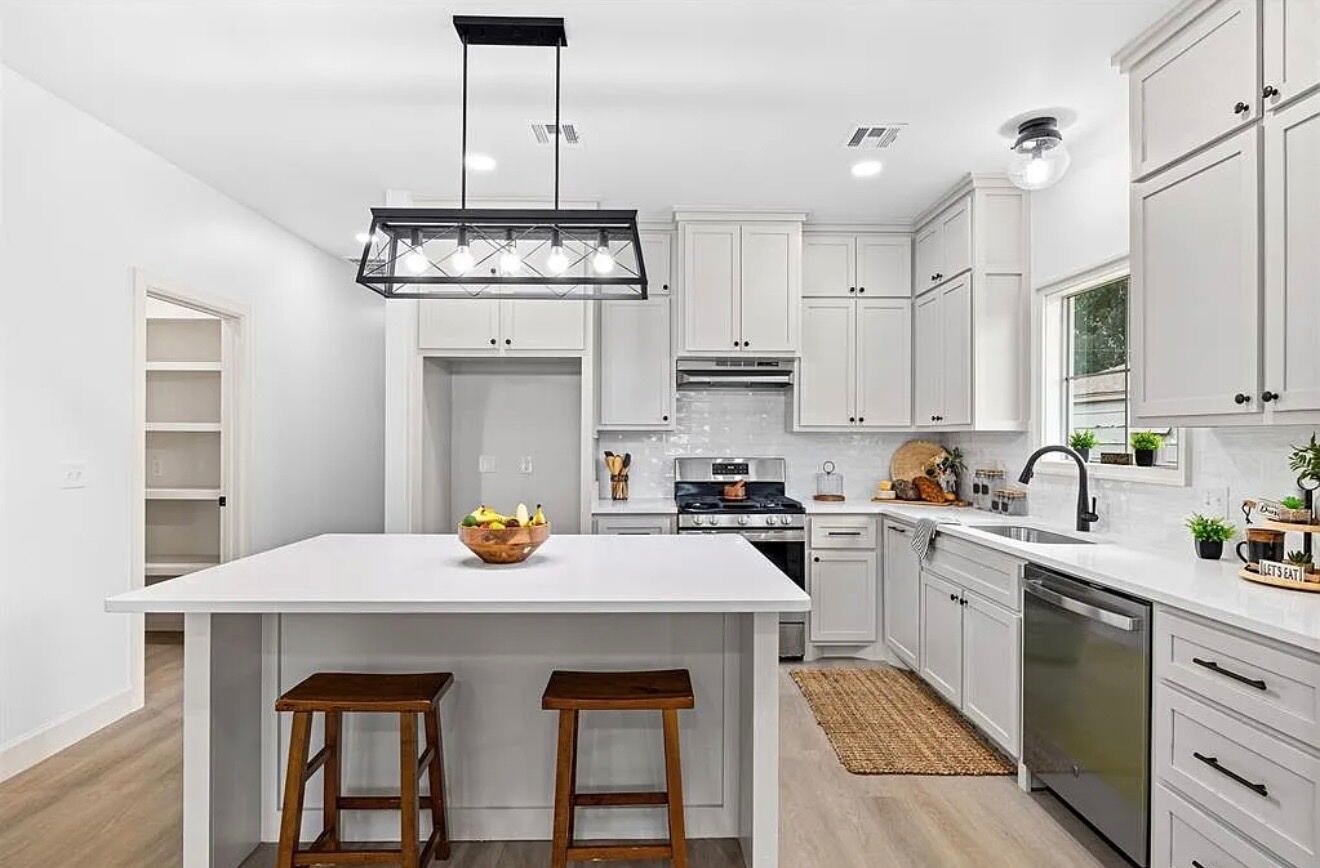 Finished white shaker kitchen with large quartz island, farmhouse pendants, and dark wood floors.
